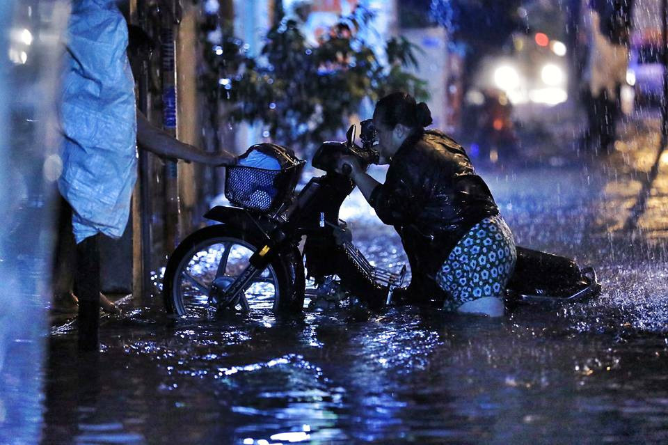 Sau một lúc hì hục không thể đẩy chiếc xe máy lên cầu thang cao hơn nửa mét đã ngập nước, người phụ nữ phải nhờ người dân kéo phụ.  