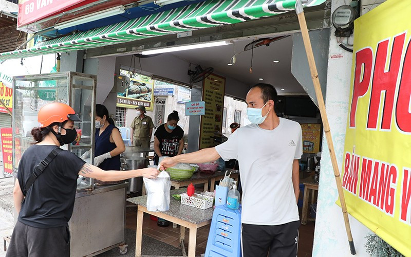 Mua đồ ăn mang về tại cửa hàng trên phố Văn Cao, quận Ba Ðình (Hà Nội) trong ngày đầu tiên được phép mở cửa trở lại. Ảnh: MINH HÀ 