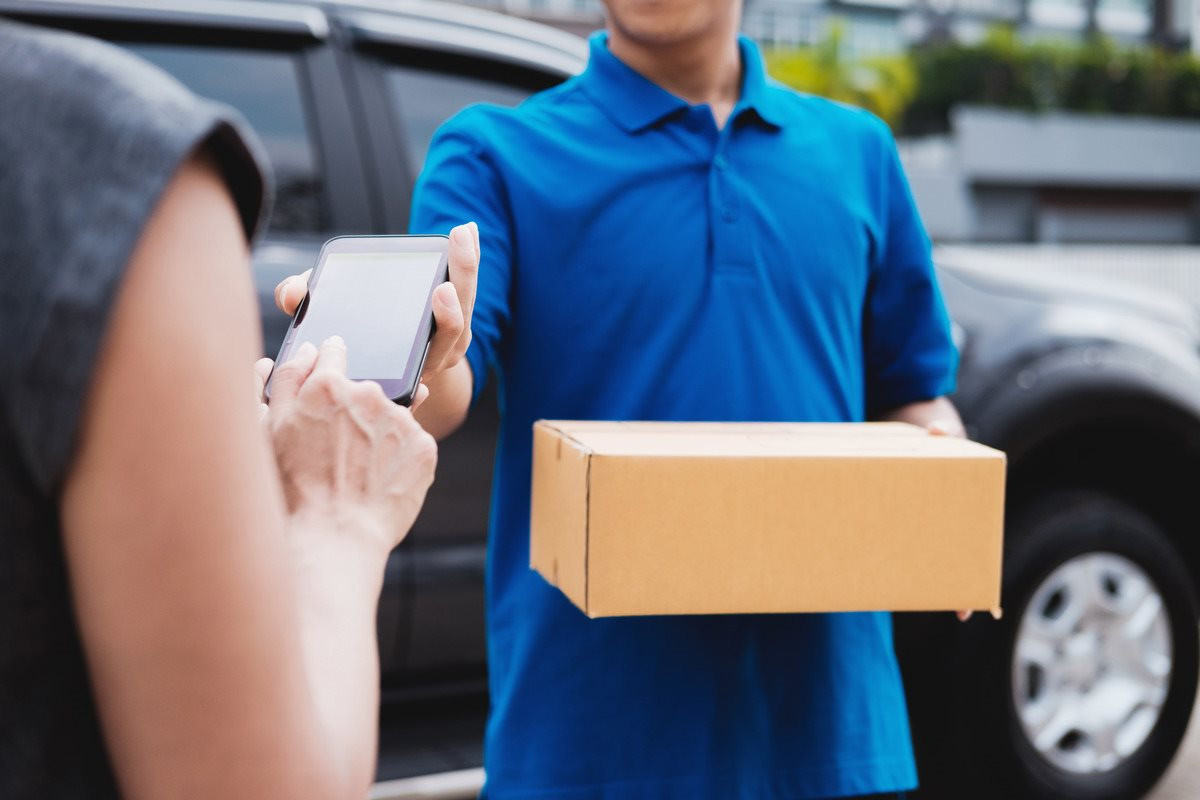 midsection-woman-holding-mobile-phone-while-delivery-man-holding-box-outdoors-1-.jpg