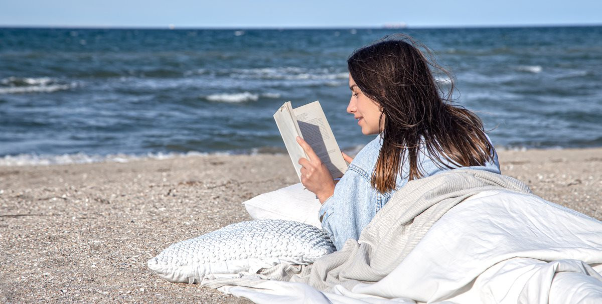 young-brunette-woman-is-lying-by-sea-beach-covered-with-blanket-reading-book-cozy-atmosphere-beach-summer-concept-1-.jpg